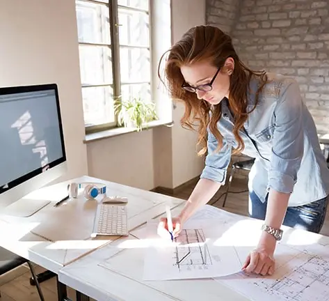 Image of a focused female designer in an office, actively working on an architect's project. Reflects the professional atmosphere of architectural workspaces, suitable for individuals seeking architecture dissertation help and inspiration for their academic projects.